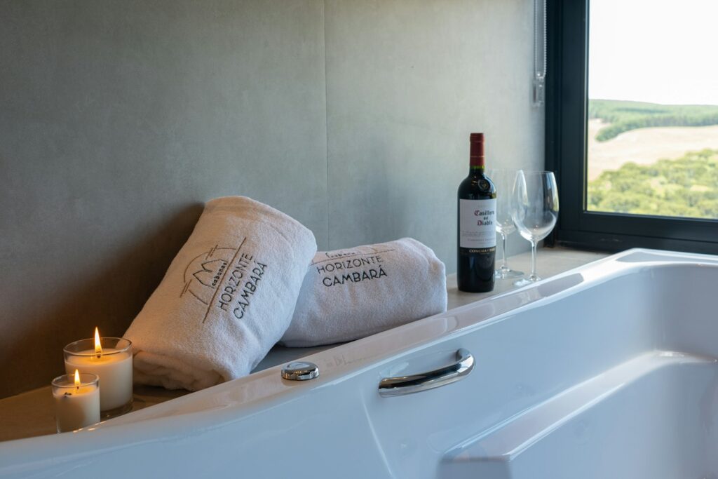 Two towels, a wine bottle and glasses beside a bathtub, set up for a spa break
