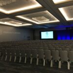 Rows of empty white chairs set out in a room before a conference, theatre style
