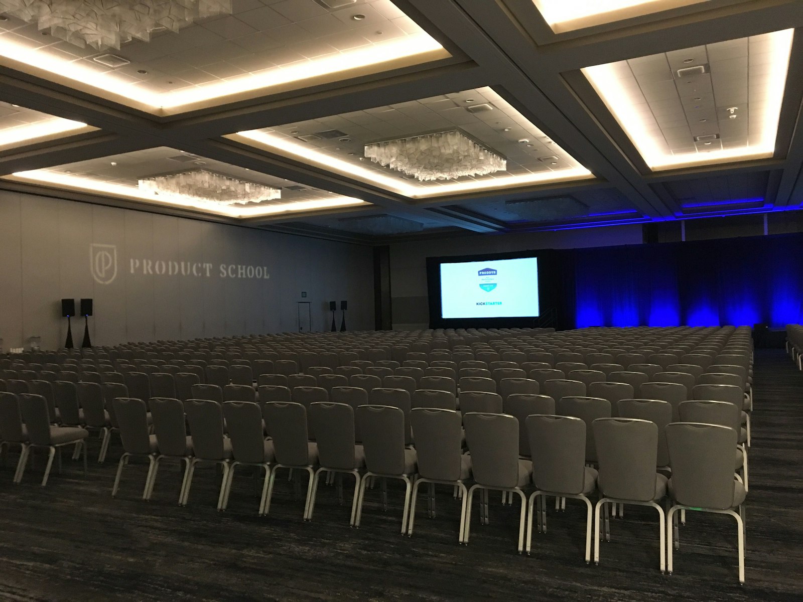 Rows of empty white chairs set out in a room before a conference, theatre style