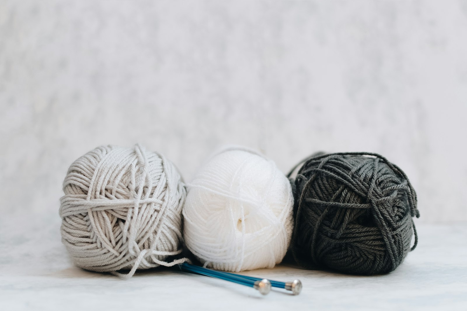 Balls of white, grey and black yarn alongside knitting needles, ready for a summer project